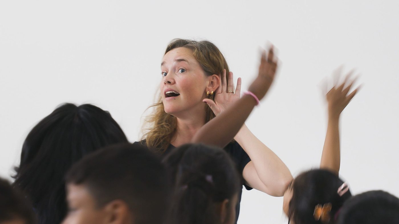 A Seanse teaching artist cups her ear as children raise their arms during the My Childhood Project in India